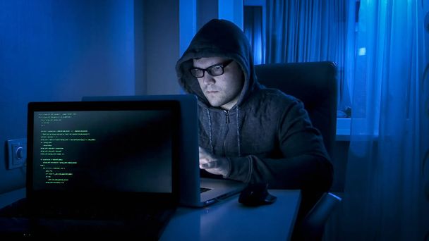 Porträt eines jungen männlichen Hackers, der nachts von zu Hause aus arbeitet - Foto, Bild