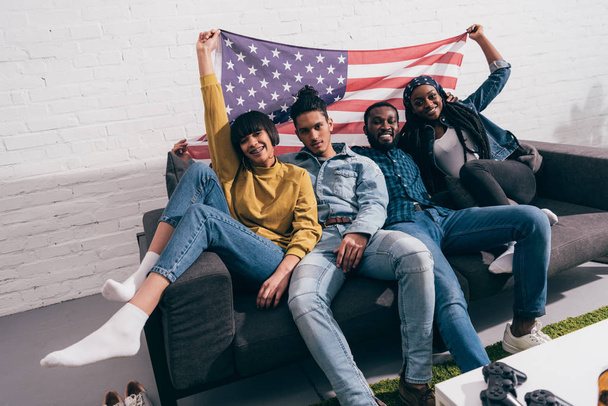 Gruppe junger multikultureller Freunde sitzt auf Couch mit US-Fahne - Foto, Bild