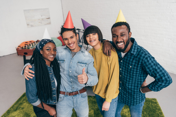 Junger Mann mit gemischter Rasse steht mit Freunden in Partyhüten auf  - Foto, Bild