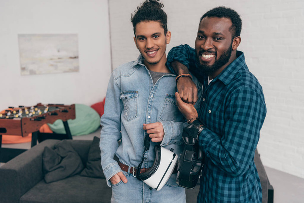 two smiling multicultural young male friends standing with virtual reality headsets - Fotoğraf, Görsel