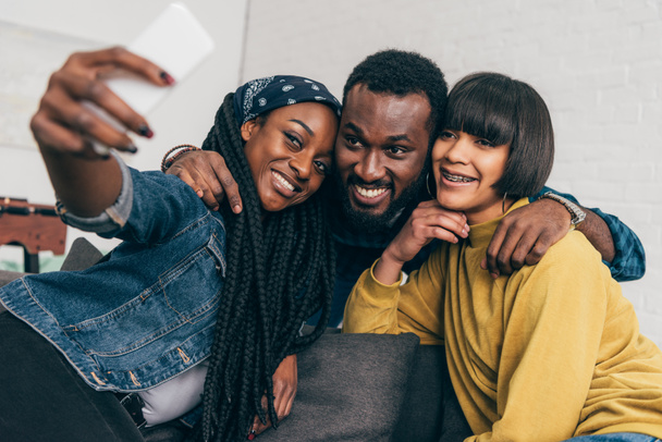 sonriente mujer negra tomando selfie con dos amigos multiétnicos
 - Foto, imagen