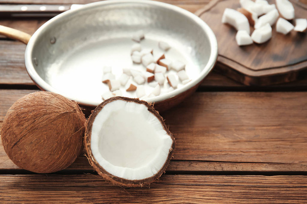 Frying pan with coconut pieces on wooden background - Foto, afbeelding