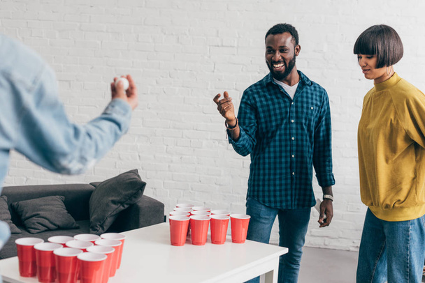 cropped image of multiethnic group of friends playing beer pong at table  - Photo, Image