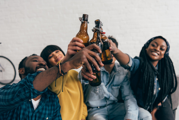 smiling multicultural friends clinking bottles of beer  - Фото, зображення