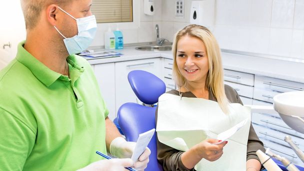 Hombre dentista dando prescripción a hermosa joven sentada en silla de dentista
 - Foto, Imagen