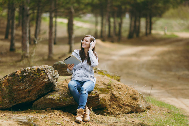 junge, entspannt lächelnde Frau in lässiger Kleidung auf Stein sitzend  - Foto, Bild