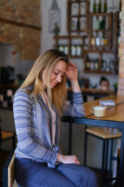 異常なインテリアと居心地の良いカフェでカプチーノのカップとテーブルのそばに座って満足している女の子. - 写真・画像