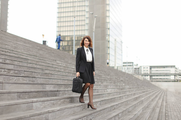 Caucasian businesswoman going down on stairs in high buildings background. - Photo, Image