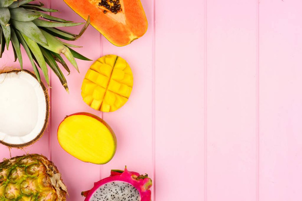 Tropisch fruit zijrand met ananas en dragon fruit, papaja, kokosnoot, mango op een roze houten achtergrond - Foto, afbeelding