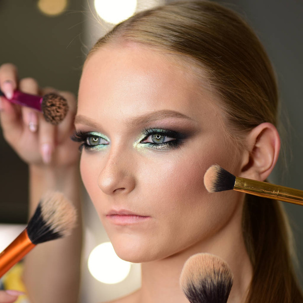 Girl getting powder on skin with makeup brushes. Girl with getting makeup on face. - Foto, Imagen
