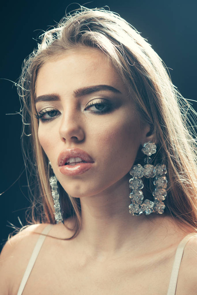 Professional makeup concept. Beauty fashion sexy girl with makeup, lipstick, eyeshadow, mascara, wears big earrings jewelry, dark studio background. Woman with sensual lips looks attractive. - Foto, imagen