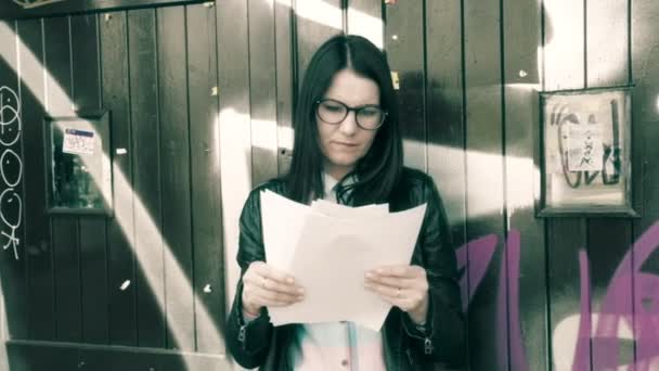 Girl on graffiti background in glasses and shirt looking documents, reports, tests. - Video, Çekim