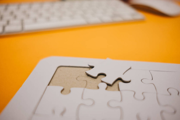 business background white jigsaw placed on orange table with clock, keyboard and copy space. image for texture, problem, thinking, idea, toy, time, workspace, success, game concept - 写真・画像