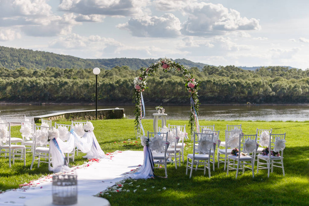 川。ロマンチックな結婚式。リボンと緑の芝生の上に花で白い木製の椅子。お客様の素敵なアームチェア - 写真・画像