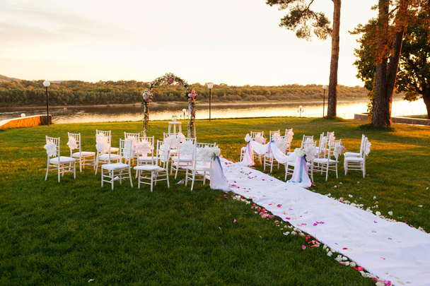 günbatımı Nehri üzerinde. Romantik düğün töreni. Şerit ve çiçeklerle bir yeşil çim üzerinde beyaz ahşap sandalyeler. Konuklar güzel Ofis koltukları - Fotoğraf, Görsel
