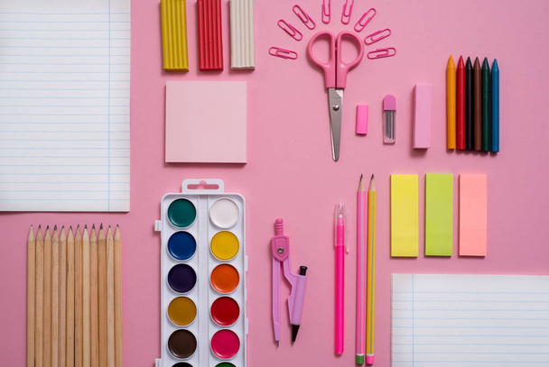 On a pink background, school accessories and a pen, colored pencils, a pair of compasses, a pair of compasses, a pair of scissors. Copy space, top view - Photo, Image