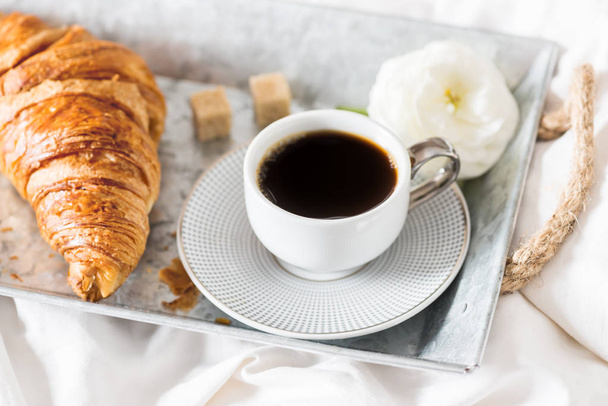 Croissant fresco, taza de café y flores de Ranunculus. Desayuno
 - Foto, imagen
