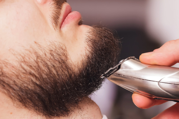 Corte uma barba com uma máquina de barbear em uma barbearia por um estilista profissional
 - Foto, Imagem