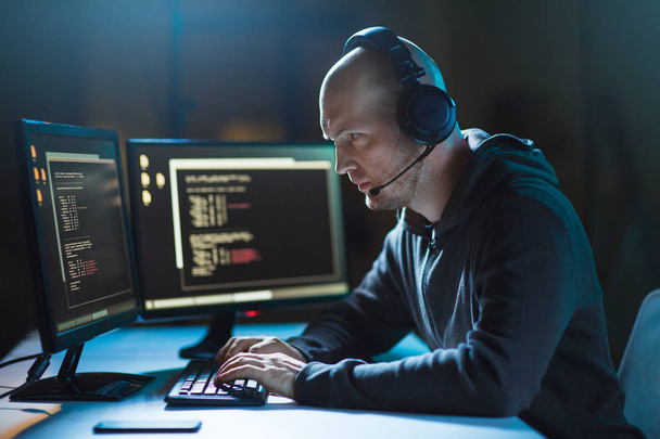 hacker with computer and headset in dark room - Foto, afbeelding