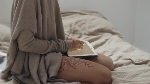 Student girl is sitting on a bed and drawing on a graphic tablet by stylus pen - Imágenes, Vídeo
