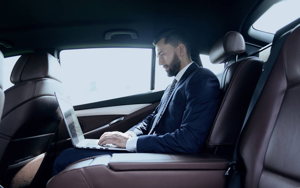 Liikemies käyttää kannettavaa tietokonetta auton takapenkillä
 - Valokuva, kuva