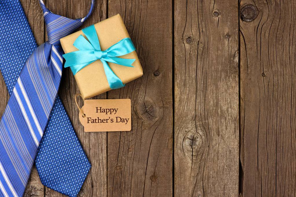 Happy Fathers Day etiqueta de regalo con regalo y lazos borde lateral sobre un fondo de madera rústica. Vista superior con espacio de copia
. - Foto, Imagen
