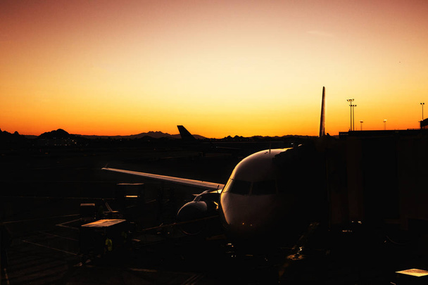 Silhouette of commercial airplane with highlight on one side from a golden sunrise at an airport in Phoenix Arizona, USA - Photo, Image