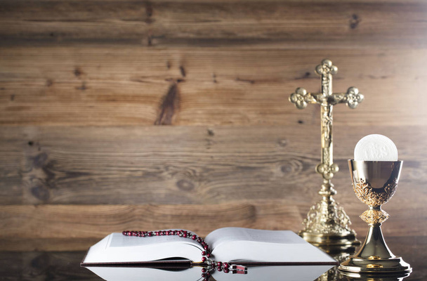 Thema der Erstkommunion. Kreuz, Bibel, Rosenkranz und goldener Kelch auf braunem Hintergrund. - Foto, Bild