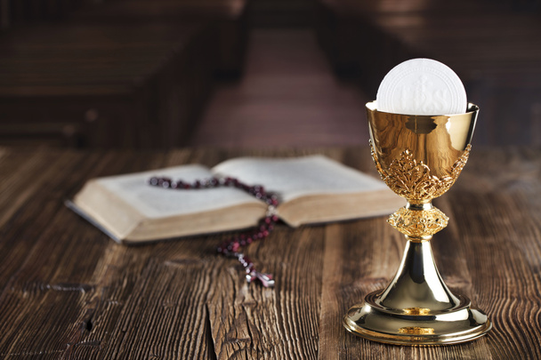 Thema der Erstkommunion. Bibel, Rosenkranz und goldener Kelch auf braunem Hintergrund. - Foto, Bild