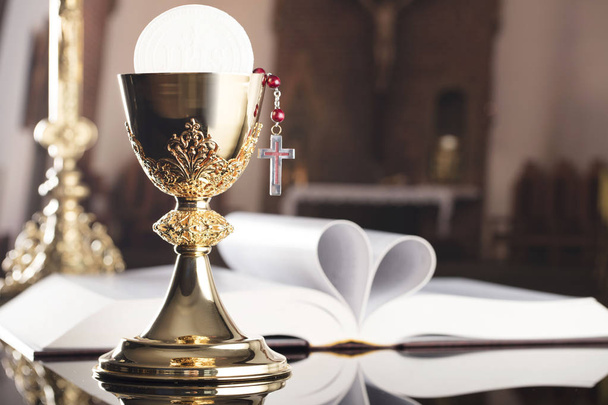 最初の聖体拝領のテーマ。十字架、聖書、ロザリオ、祭壇の上の黄金の杯. - 写真・画像
