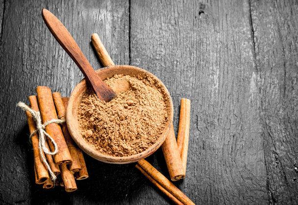 Ground cinnamon in a bowl. On a black wooden table. - Photo, Image