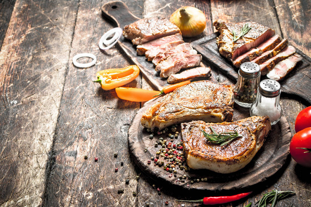 Grilled meat on the old boards with spices. On wooden background. - Photo, Image