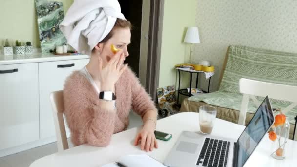 attraktive Geschäftsfrau, die zu Hause kosmetische Gesichtsflecken aufträgt und hinter dem Laptop arbeitet - Filmmaterial, Video