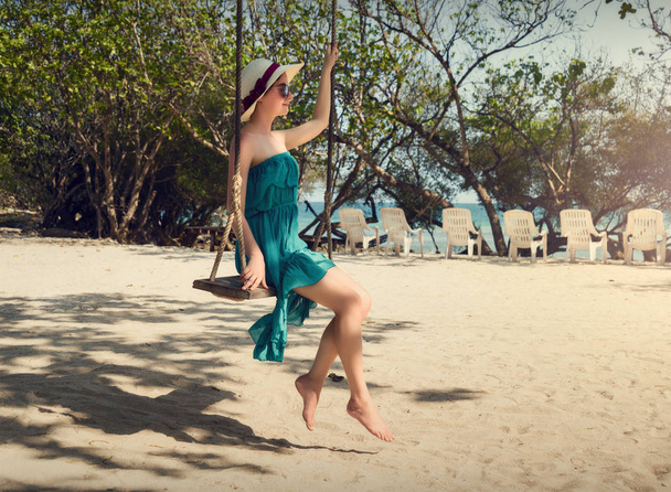 Meisje op een schommel swingen. Een meisje in een hoed en een jurk. Strandvakantie. - Foto, afbeelding