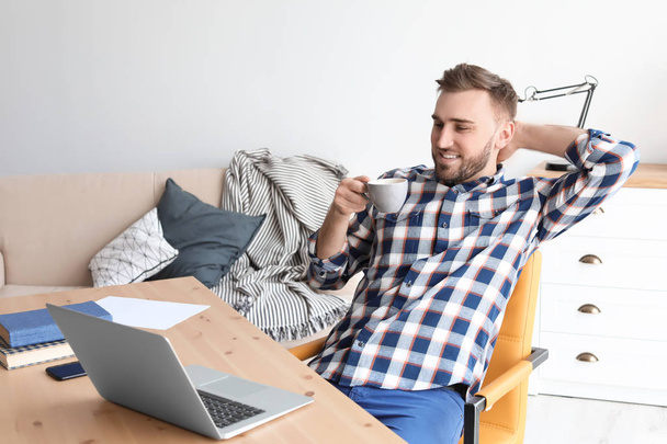 Young man drinking coffee while working with laptop at desk. Home office - Foto, afbeelding