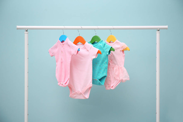 Baby clothes hanging on rack against color background - Photo, image