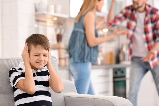 Little unhappy boy sitting on sofa while parents arguing at home - Fotó, kép