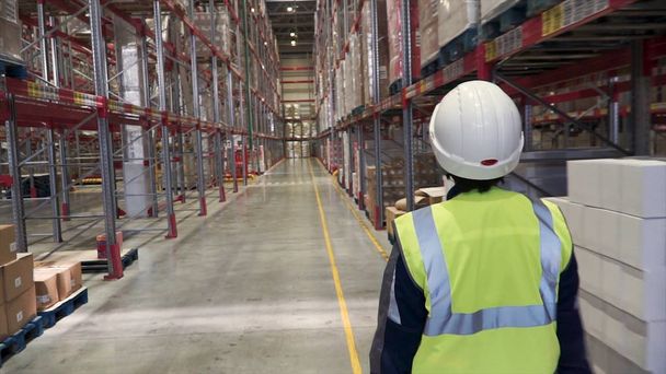 Back view portrait of warehouse manager and worker in hardhats doing stock inventory in warehouse, looking up at tall shelves with goods. Clip. Warehouse worker on hoverboard - Photo, Image