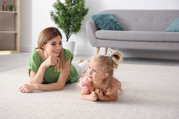 Cute little girl and her mother lying on cozy carpet at home - Photo, Image