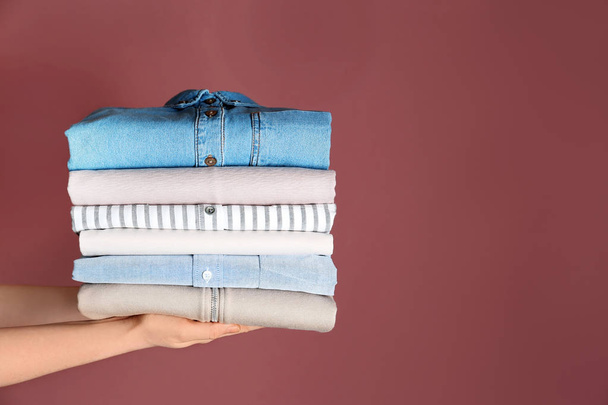 Woman holding stack of clean clothes on color background - Фото, зображення