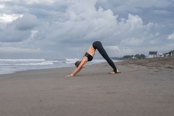 fiatal nő gyakorló jóga a Downward néző kutya jelentenek (Adho Mukha Svanasana) a tengerparton - Fotó, kép