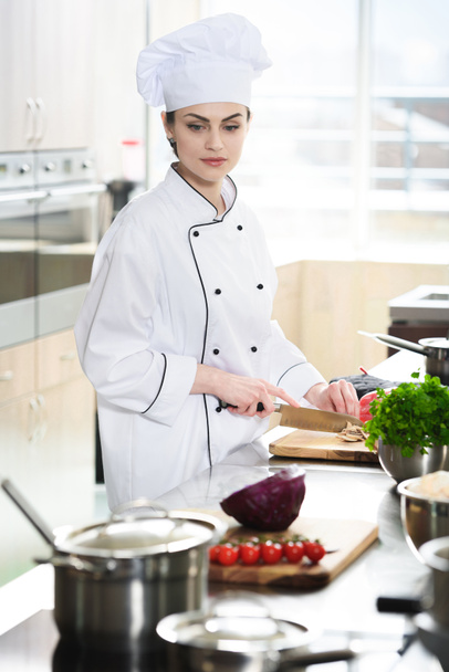 Profi-Köchin in Uniform schneidet Zutaten auf Küchentisch - Foto, Bild