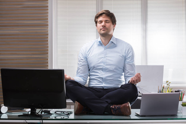 Young Businessman Sitting On Desk Meditating In Office - Фото, зображення