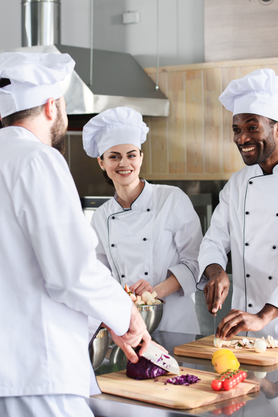 Équipe de chefs multiraciaux souriant et cuisinant sur la cuisine moderne
 - Photo, image
