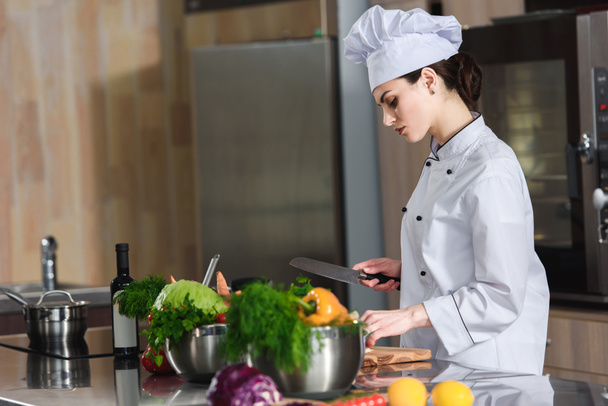 Chef femenino profesional que corta ingredientes en la mesa de la cocina
 - Foto, Imagen