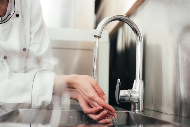Rajatut näkymät naispuolinen kokki pesu kädet yli keittiön pesuallas
 - Valokuva, kuva