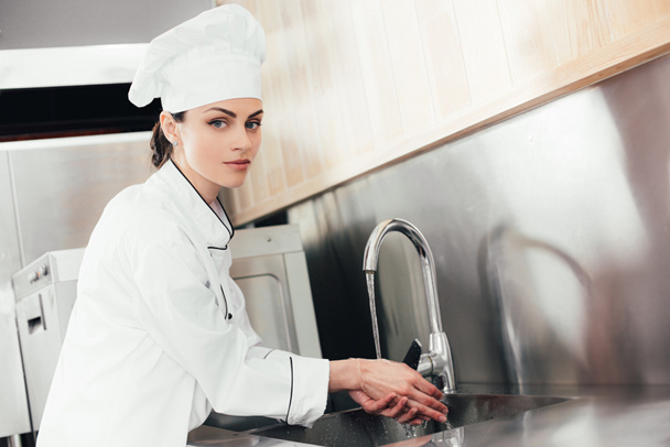 Vrouwelijke chef-kok wassen van de handen over de aanrecht - Foto, afbeelding