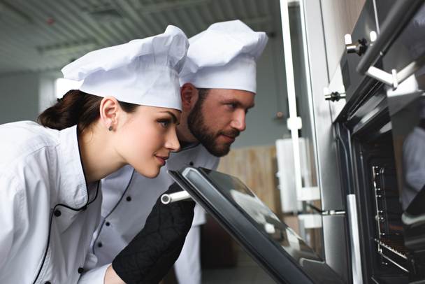 Professional chefs looking into modern kitchen oven - Photo, Image