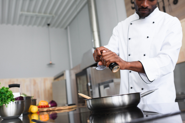 Αφρικανικός Αμερικανός σεφ καρύκευμα πιάτο με κουζίνα, ψυγείο - Φωτογραφία, εικόνα