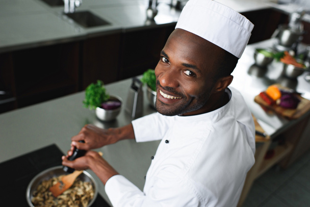 lächelnd afrikanisch-amerikanischer Koch würzt Gericht am Küchenherd - Foto, Bild